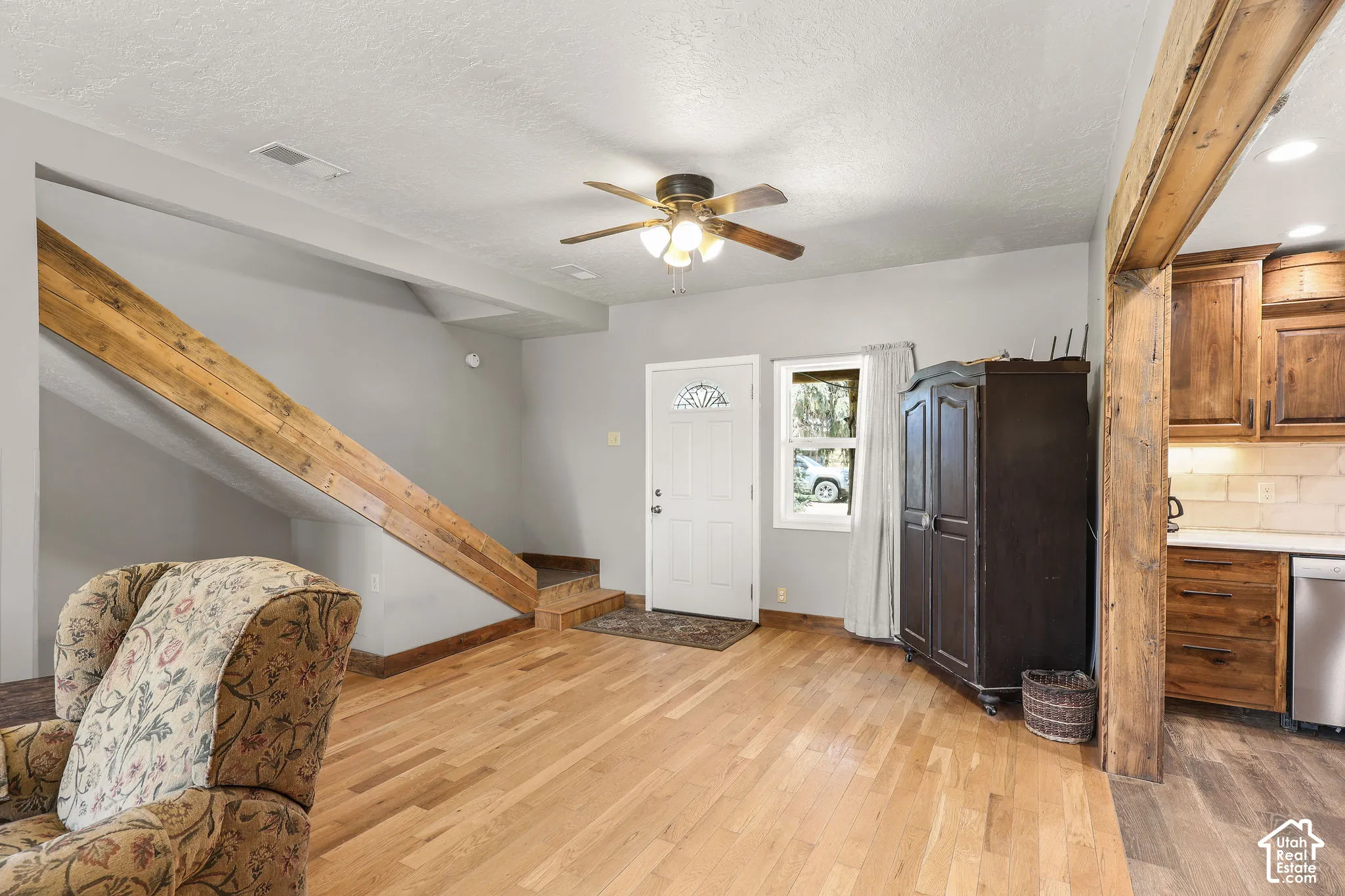Open-concept living space featuring wood-finish flooring, a ceiling fan, and a rustic wood beam framing the kitchen entry
