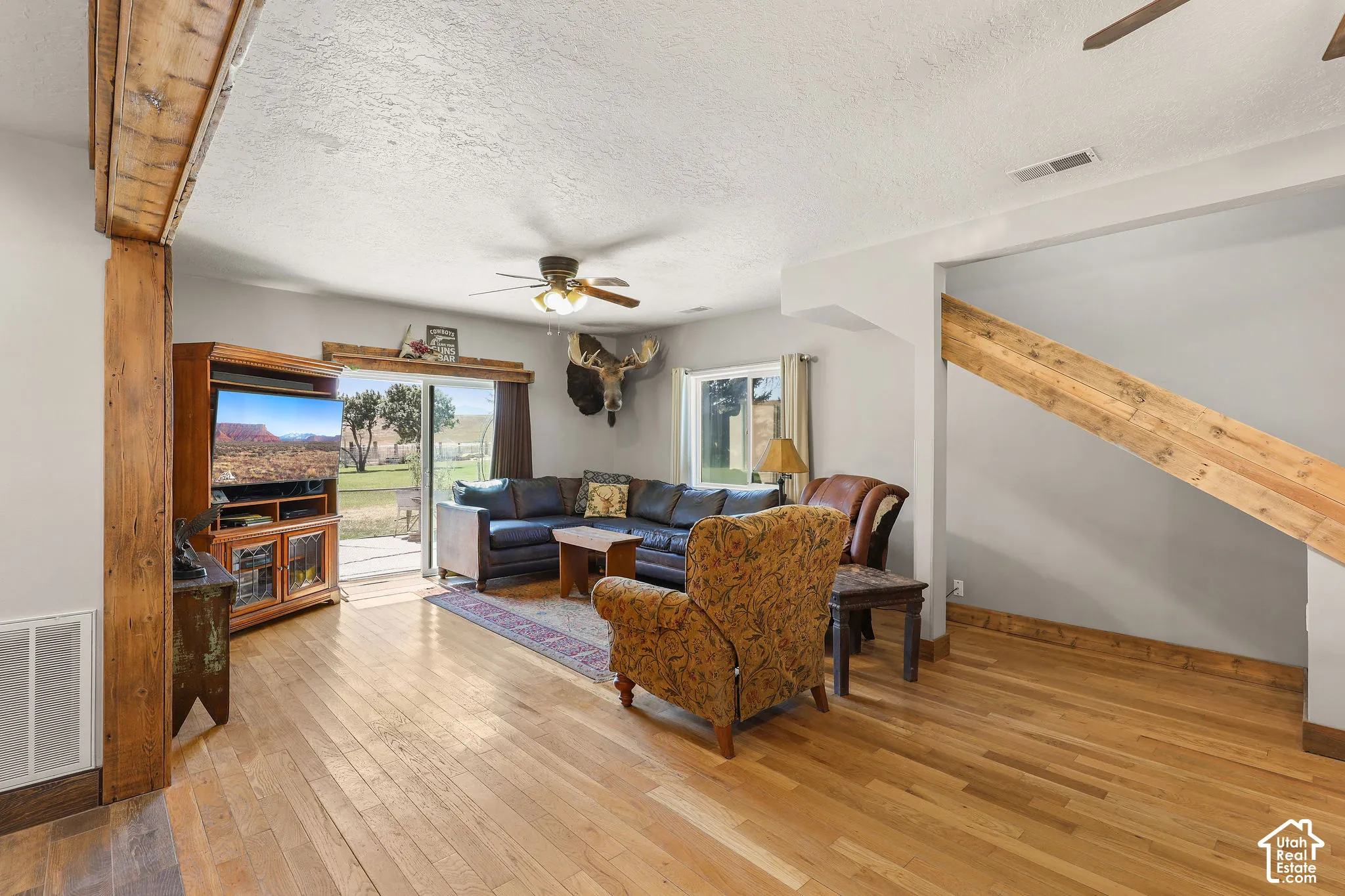 Spacious living area featuring wood-finish flooring, exposed wood beams, and a ceiling fan
