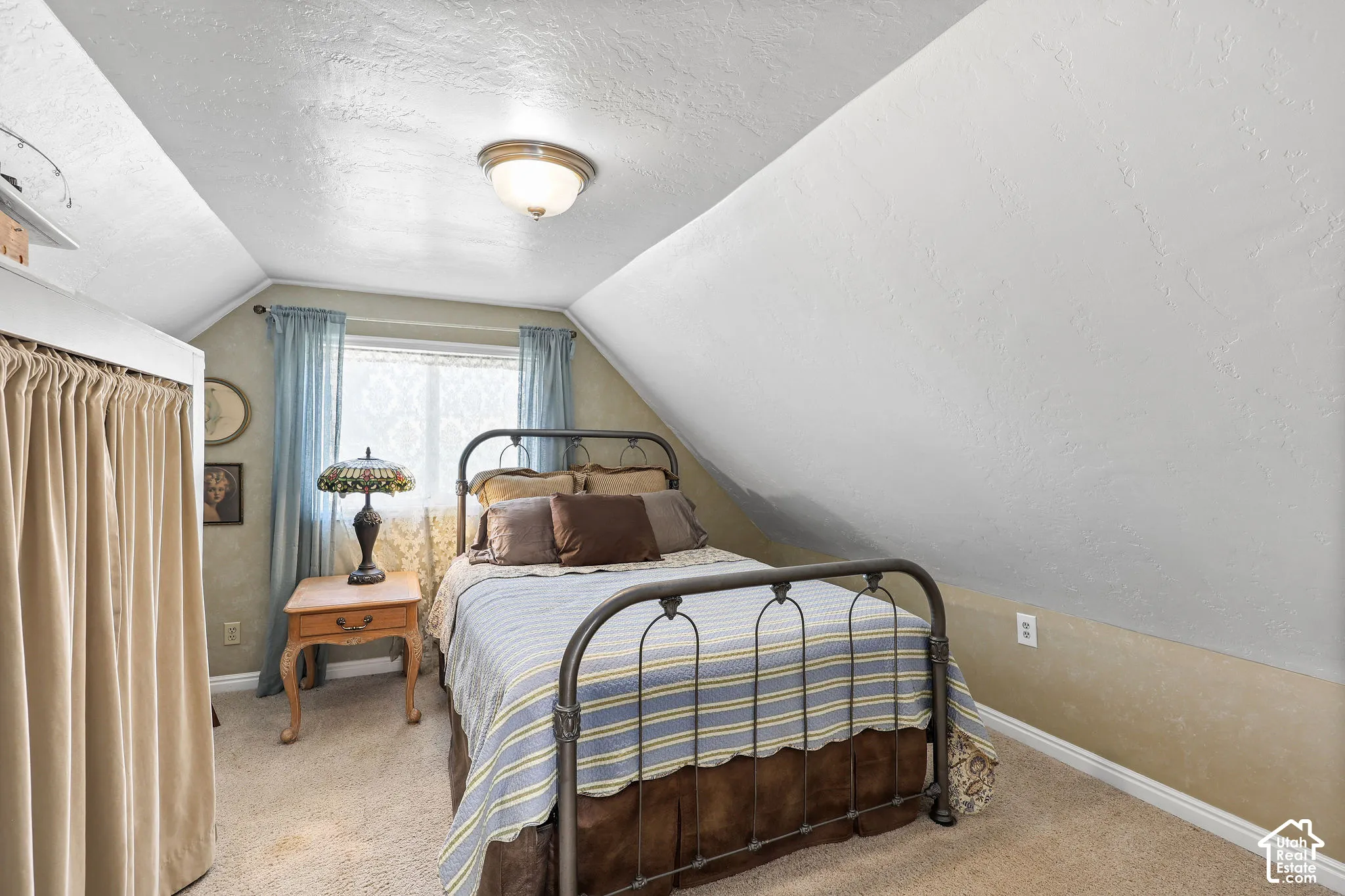 Sloped ceiling room featuring a window with privacy sheers, textured walls, a ceiling-mounted light fixture, and carpet flooring