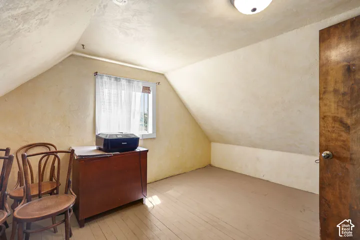 Attic room featuring sloped ceilings, painted wood-finish flooring, a single window with curtain rod, and a solid wood door