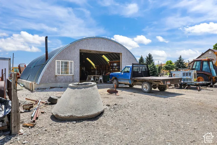 Quonset hut structure featuring a corrugated metal roof, a gravel lot, and a large garage door opening