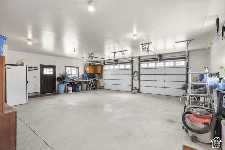 Spacious three-car garage featuring a concrete floor, two white paneled garage doors with upper window inserts, and an additional side entry door with glass panes