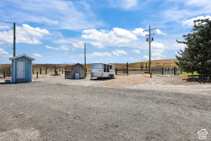 Gravel lot featuring a light blue storage shed with a white door, a rustic wooden shed, and fenced areas