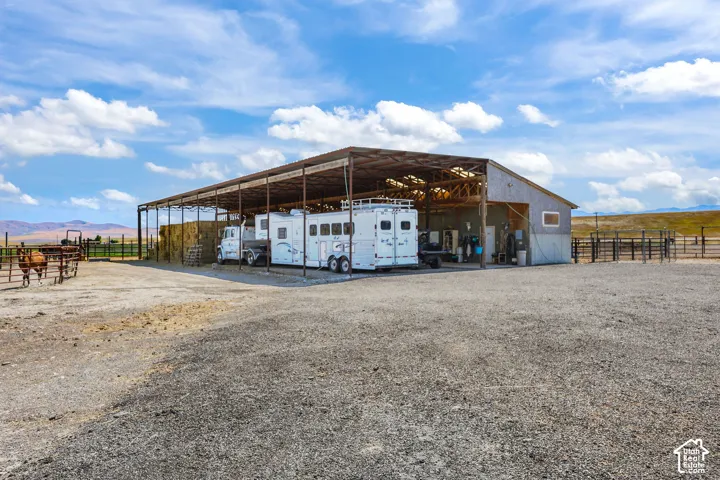 Expansive gravel lot with a large open-sided metal pole barn featuring a partial enclosed structure