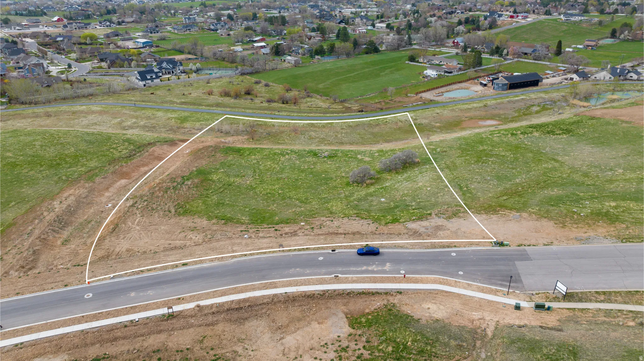 Expansive lot featuring a curvilinear paved road, concrete sidewalk, gentle slopes, and existing vegetation