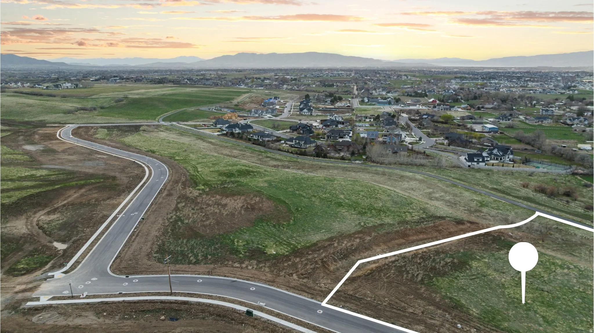 Expansive undeveloped parcel featuring a curved asphalt road frontage with integrated sidewalks