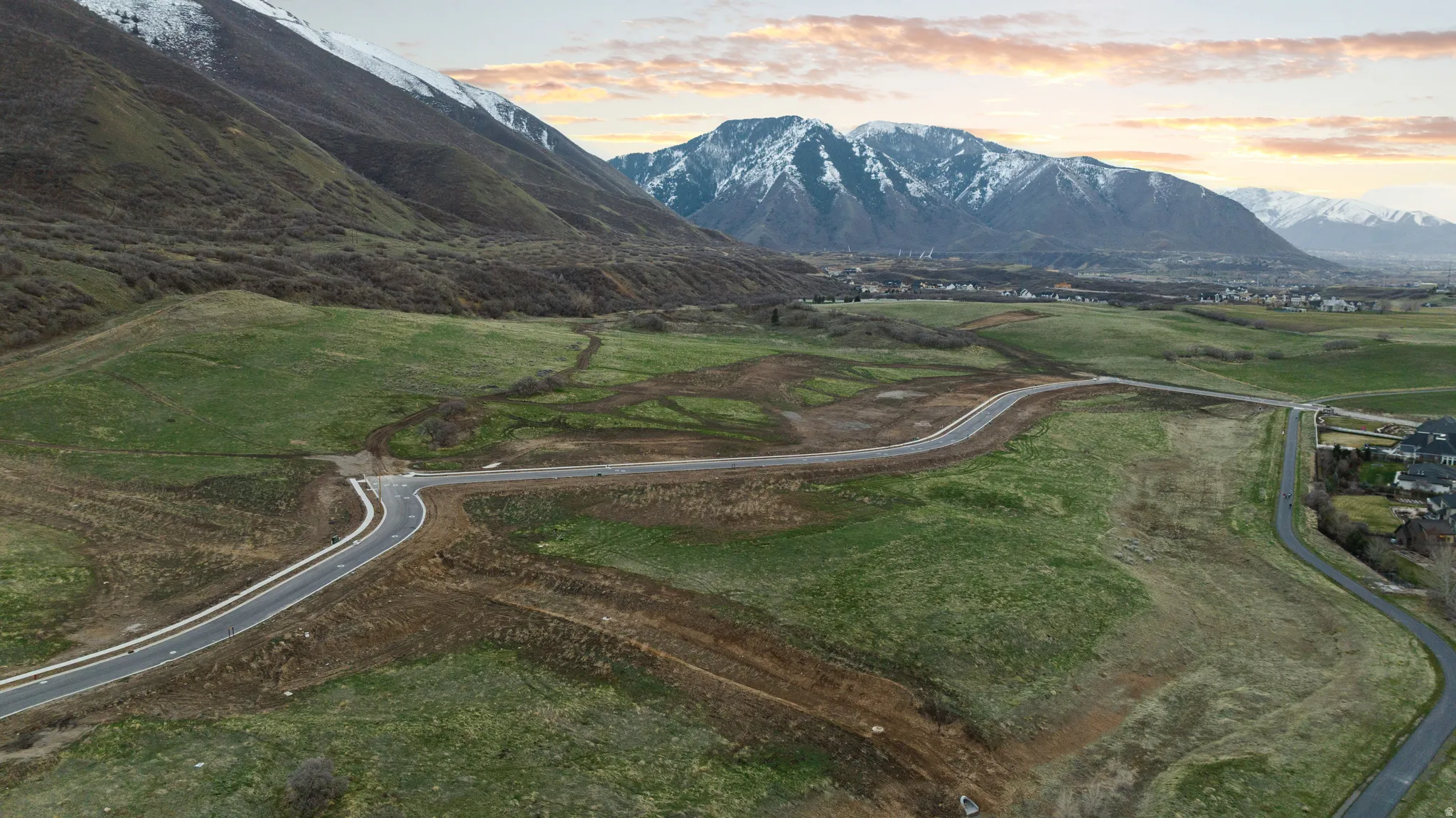 Expansive undeveloped land featuring paved roads, mountainous backdrop, and established residential areas in the distance