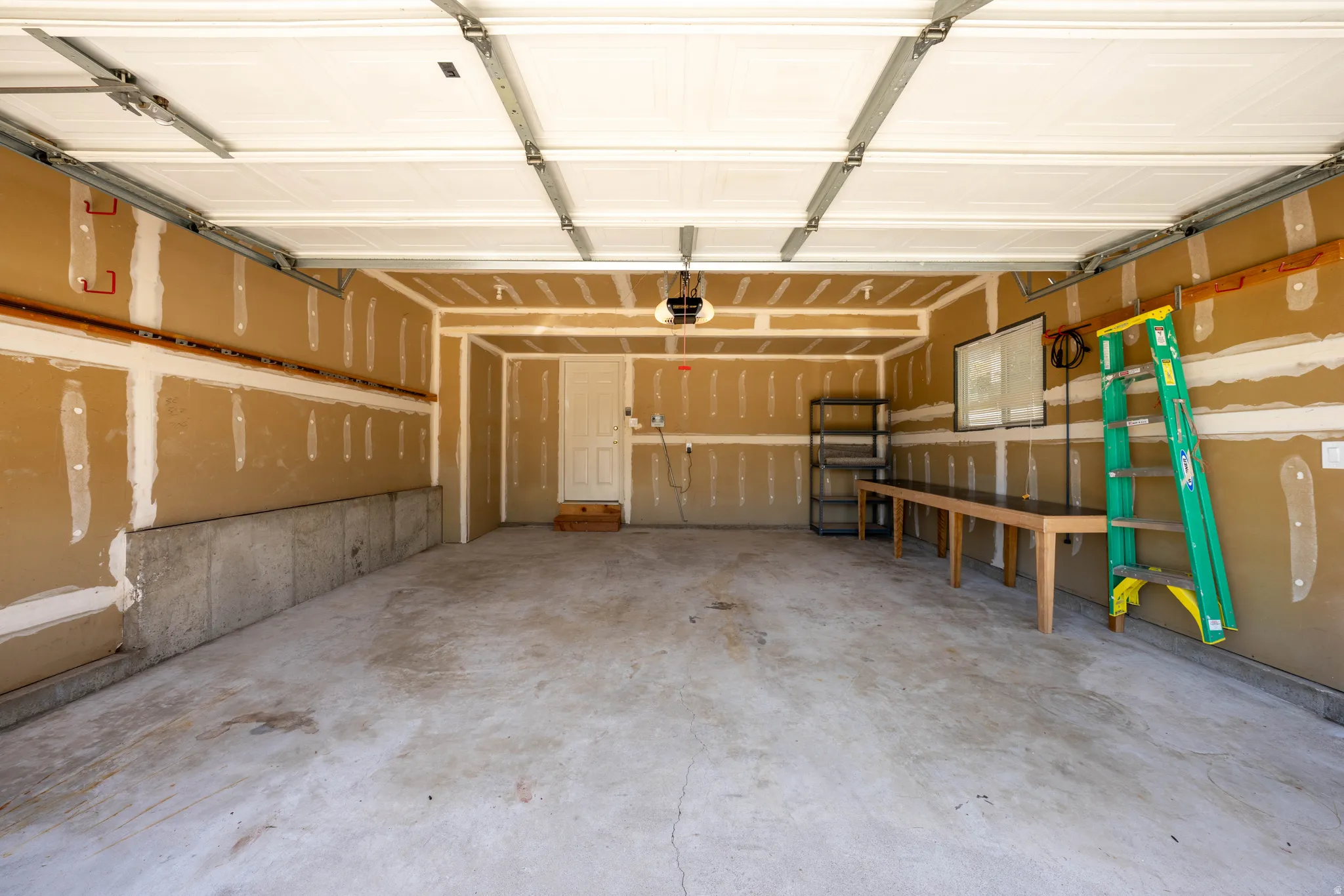 Spacious garage with concrete flooring, exposed drywall, and a white overhead garage door