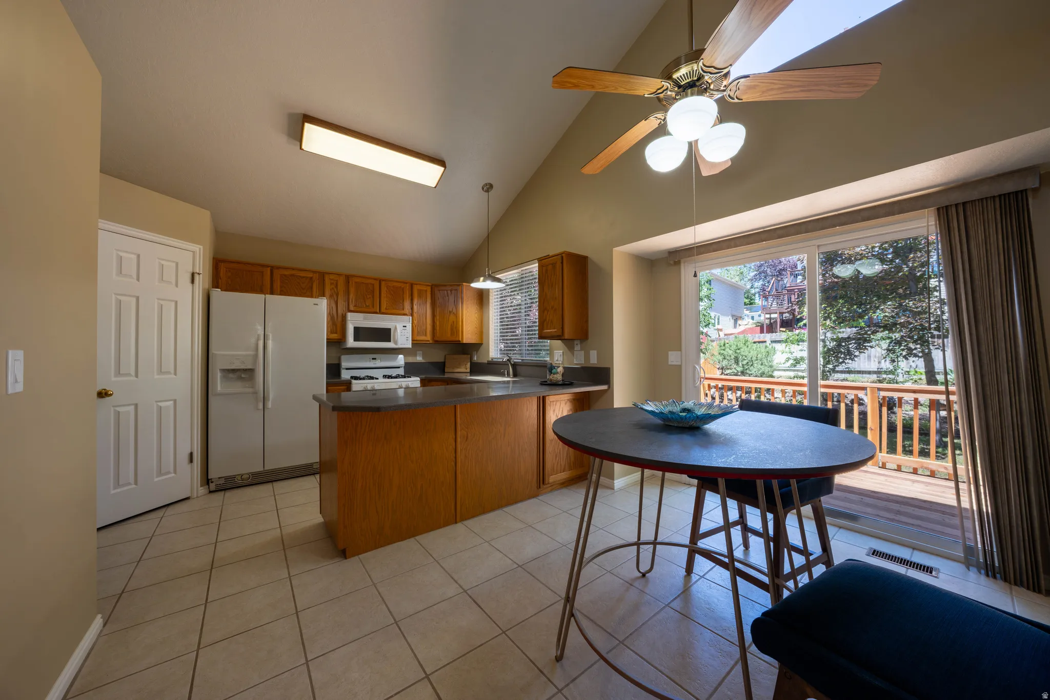 Kitchen featuring wood cabinetry, white appliances, an island with countertop seating, and tile flooring