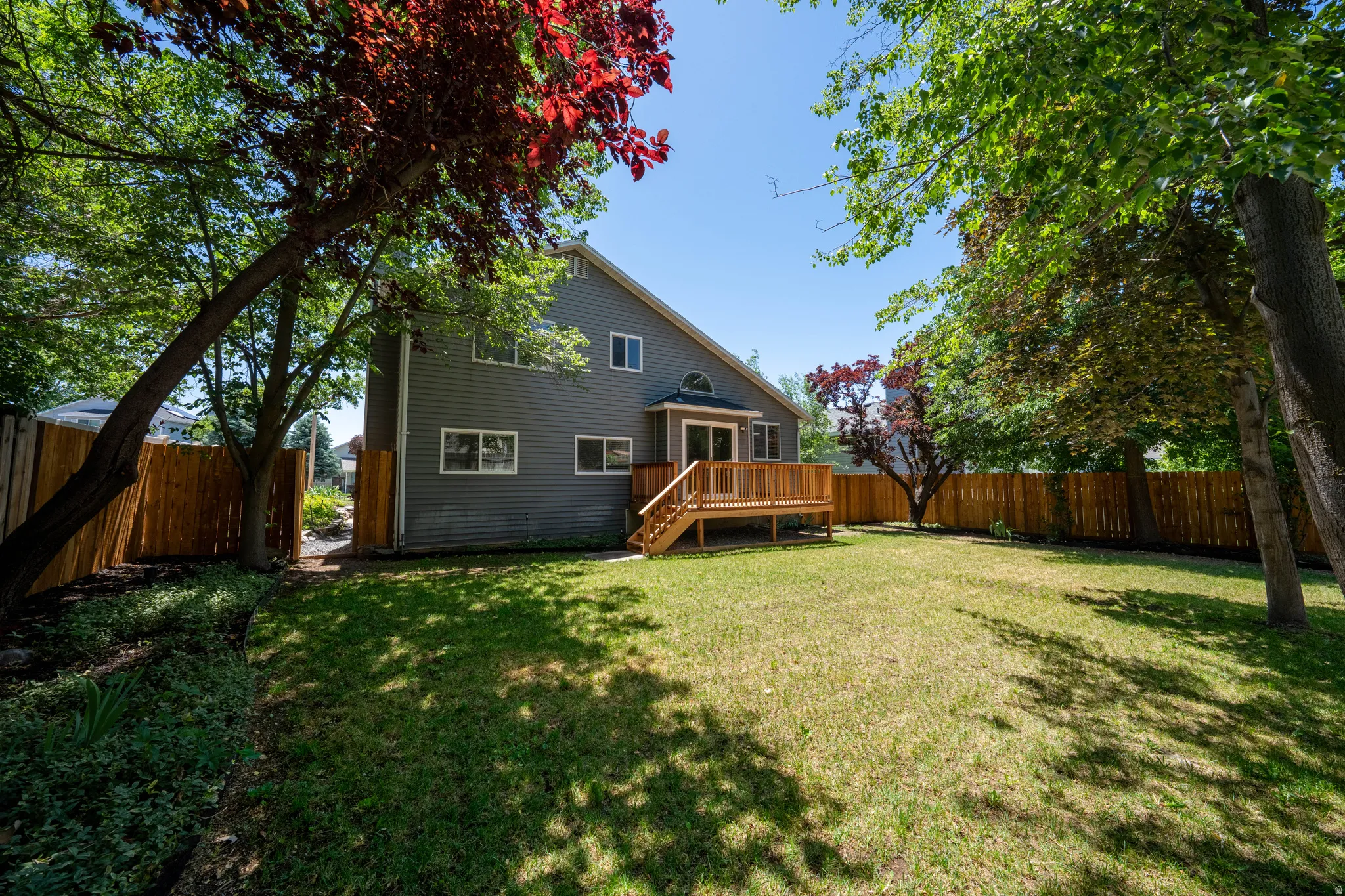 Expansive backyard featuring a manicured lawn, full privacy fencing, and mature trees