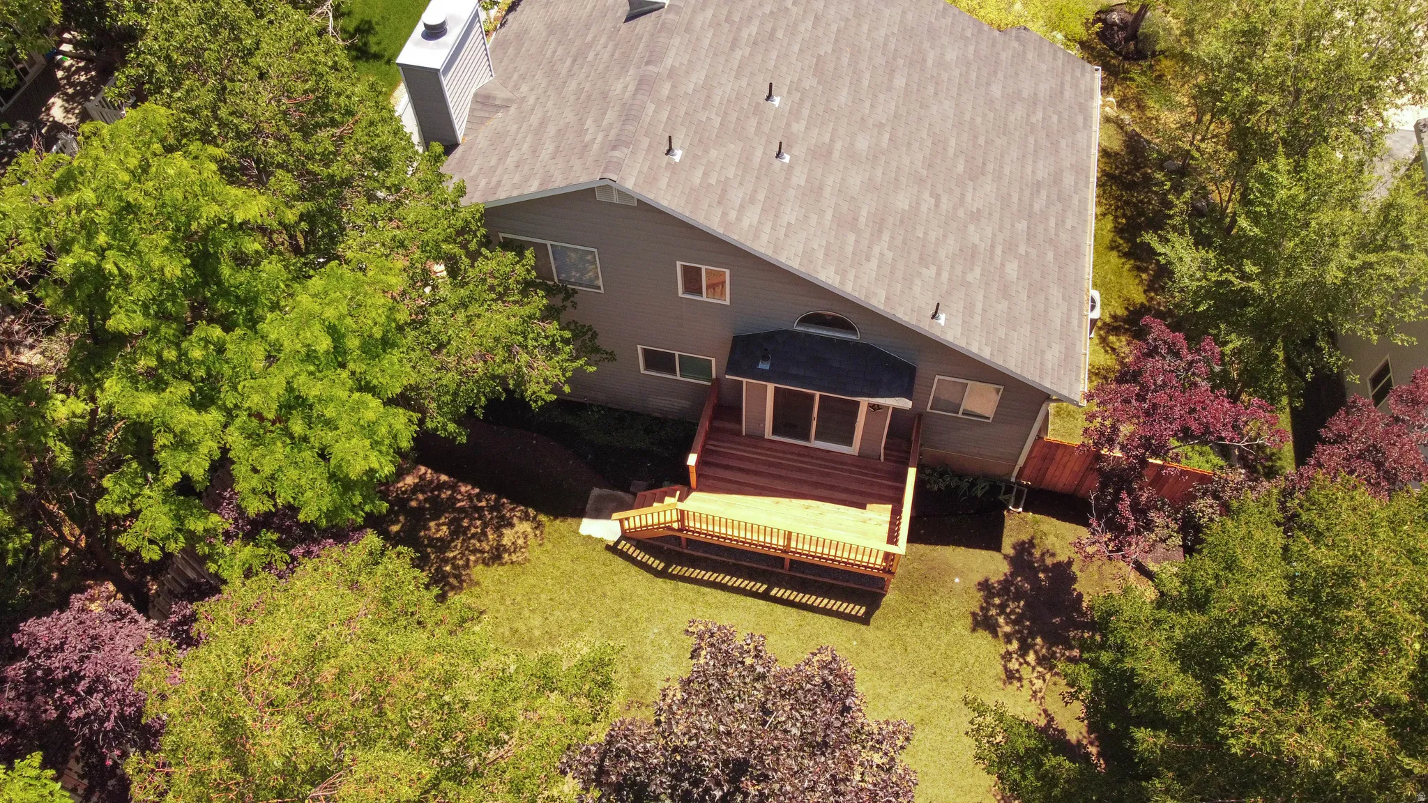 Rear exterior featuring a multi-level wood deck with railings, sliding glass doors, and a neutral-toned facade