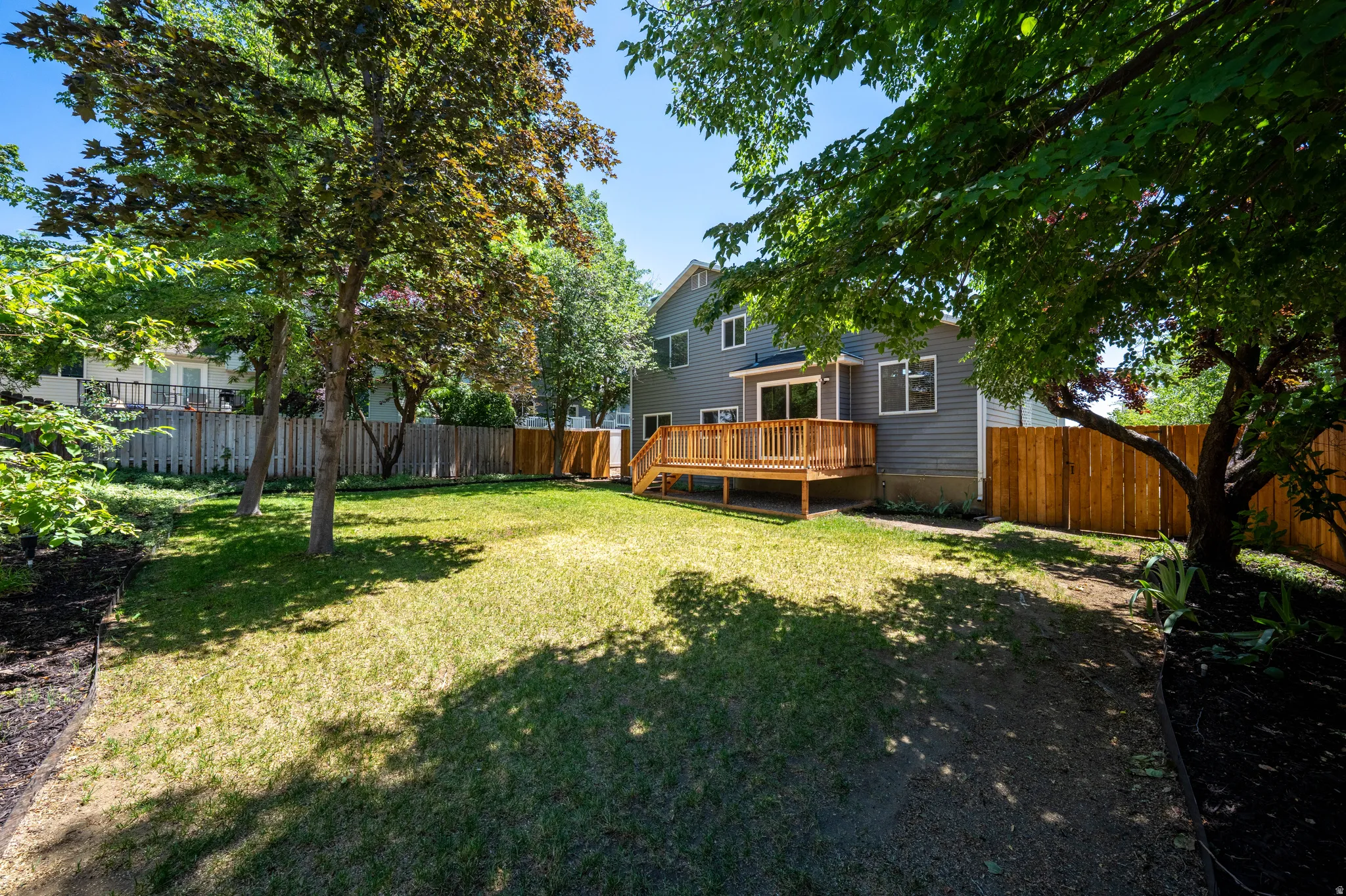 Expansive backyard featuring a manicured lawn, established trees, and a substantial wood deck