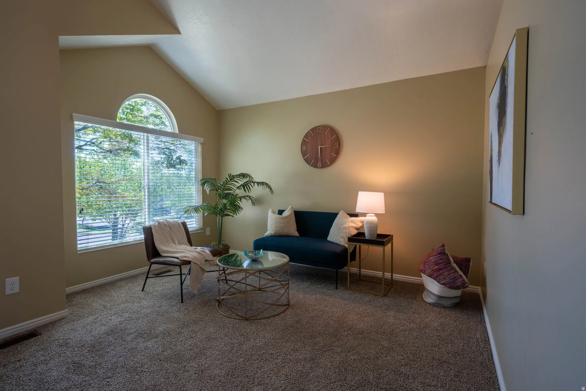 Vaulted ceiling living space featuring a large window with an arched transom, horizontal blinds, and neutral wall tones