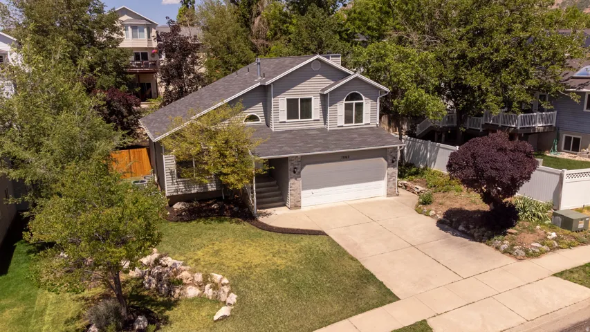 Two-story residence featuring light gray siding with stone accents, a two-car garage, and a concrete driveway