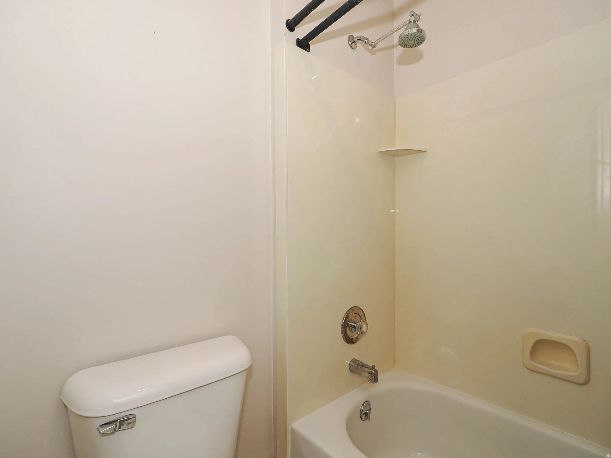 Integrated tub and shower combination featuring a beige surround, chrome fixtures, and a corner shelf