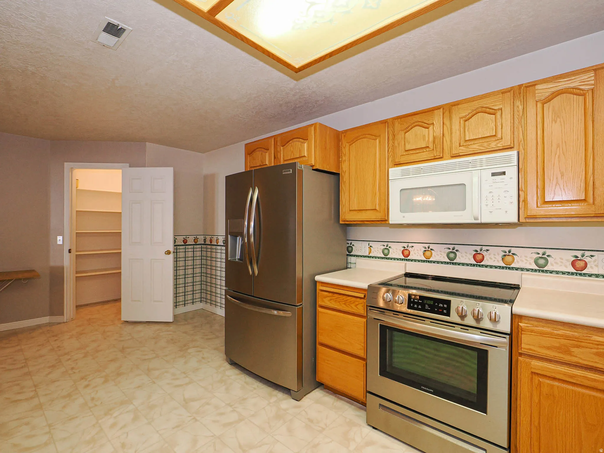 Kitchen featuring oak cabinetry, laminate countertops, a stainless steel electric range, an over-the-range microwave, and a stainless steel refrigerator