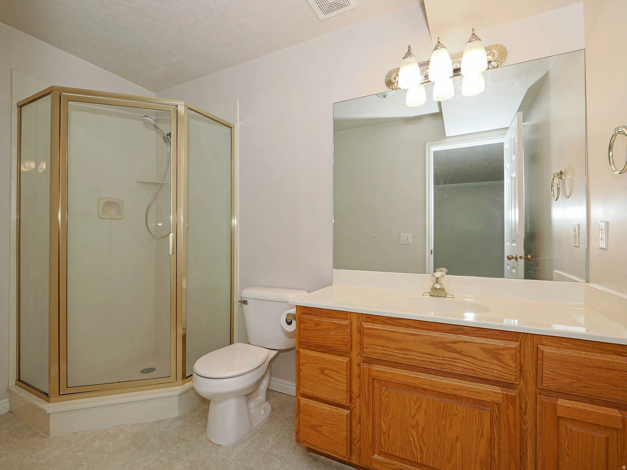 Bathroom featuring a corner shower with a gold-tone frame, a single vanity with a wood-finish cabinet, a white countertop, and an integrated sink