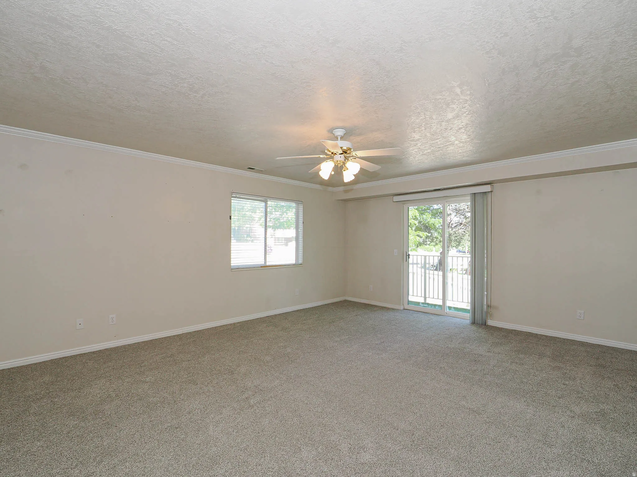 Spacious room featuring gray carpet, light-colored walls, crown molding, and a ceiling fan