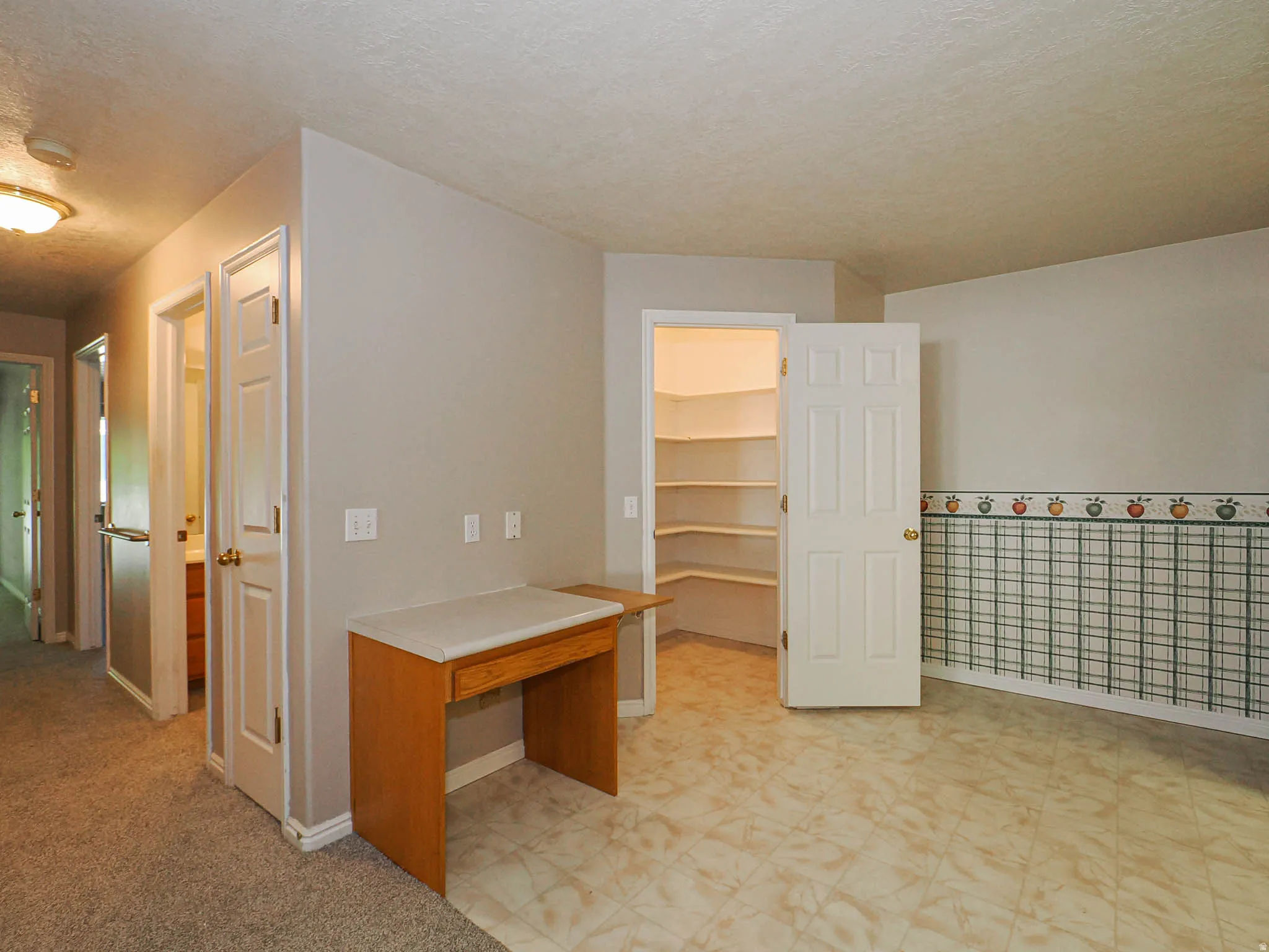 Spacious utility area featuring durable tile flooring, a built-in wood-finish desk, and a large pantry with extensive shelving