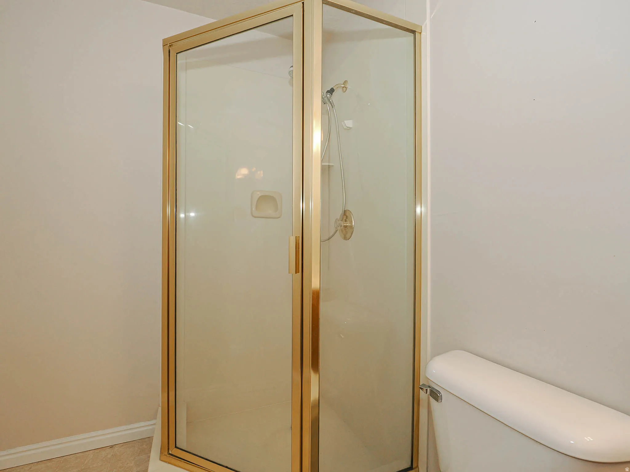 Glass-enclosed shower with a brass-finish frame and an integrated soap dish
