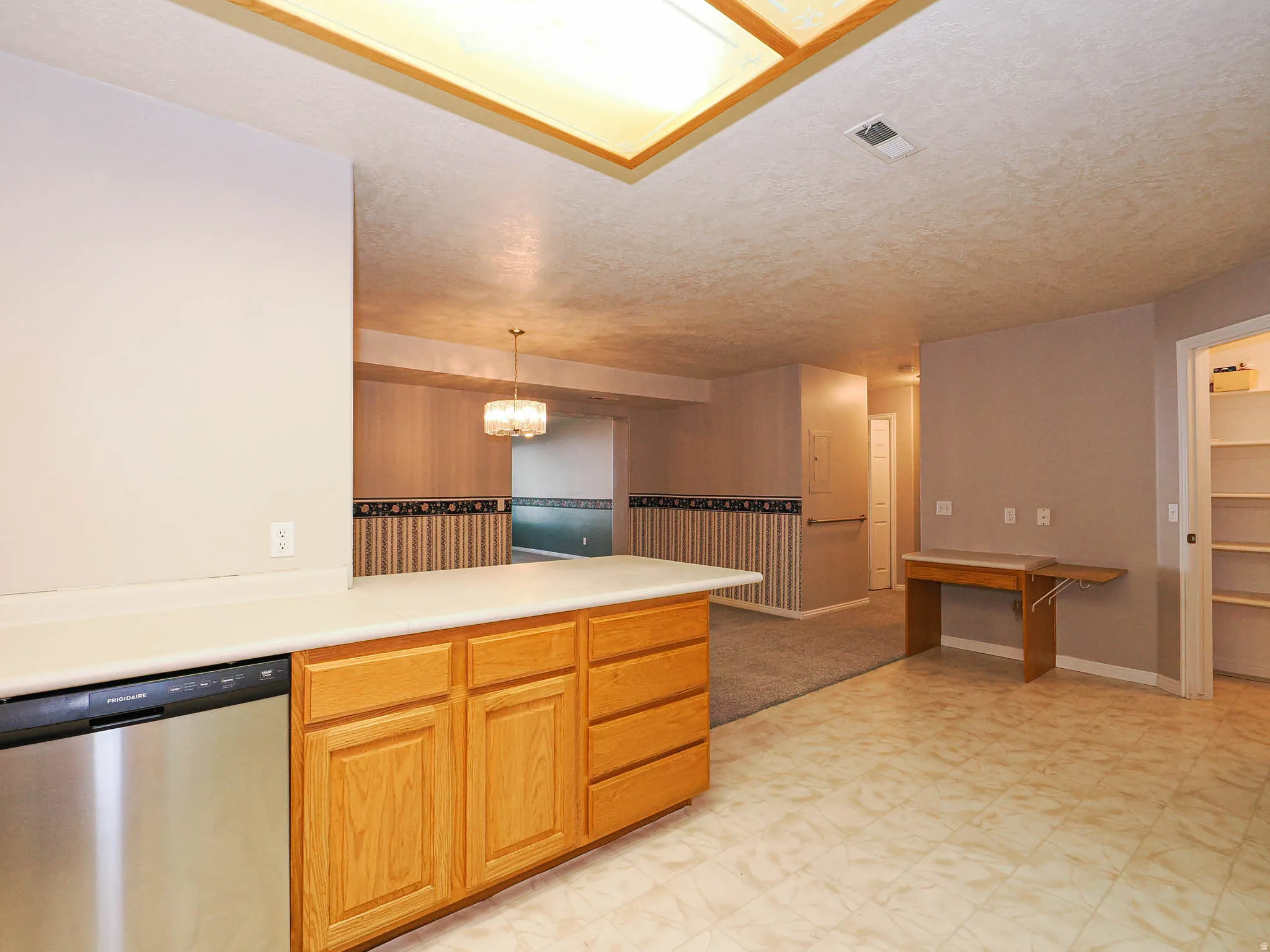 Kitchen counter with light wood cabinetry, stainless steel dishwasher, and light-toned countertop