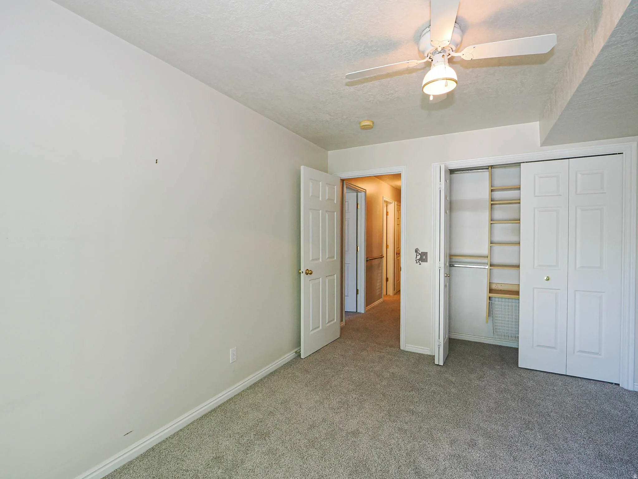 Carpeted room with a ceiling fan, bi-fold closet doors, built-in closet shelving, and a white baseboard trim