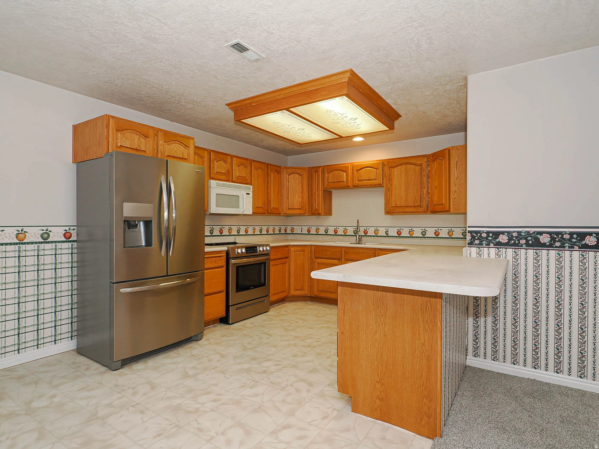 Kitchen featuring wood cabinetry, stainless steel appliances, a built-in microwave, a corner sink with a goose-neck faucet, and a peninsula countertop