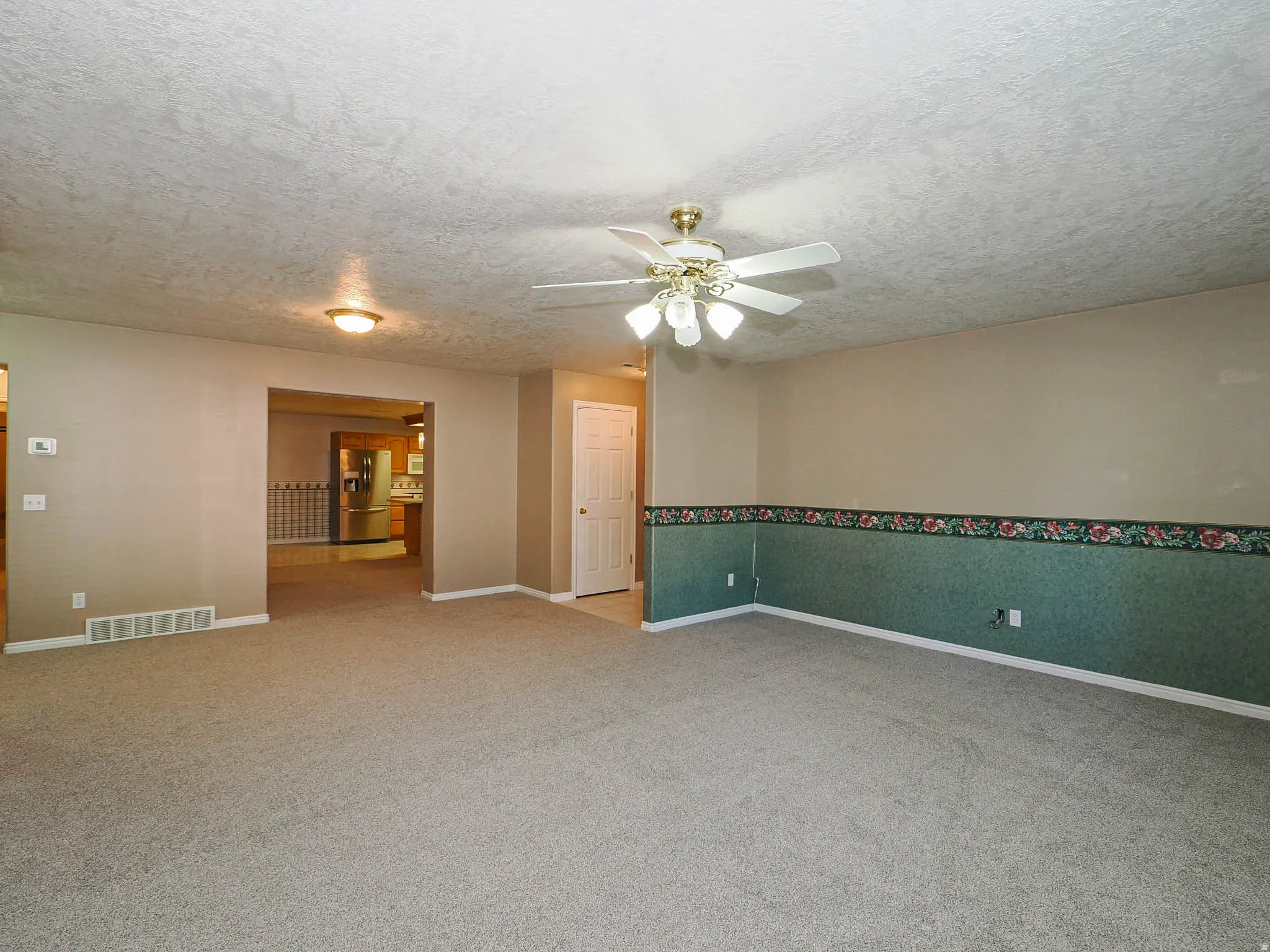 Spacious room featuring neutral carpet and a ceiling fan with light fixture