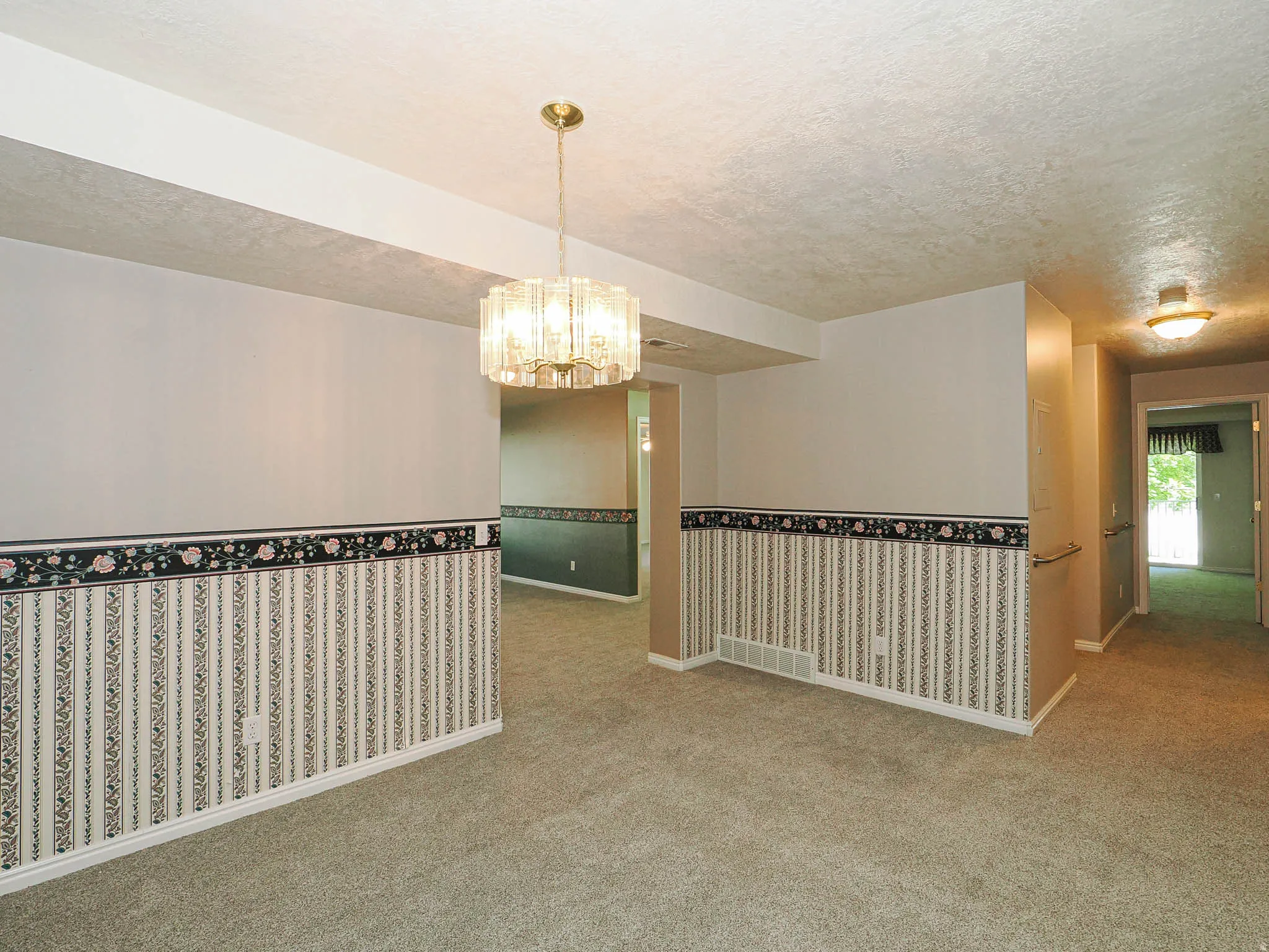 Carpeted room featuring a decorative wall border, baseboard trim, and a brass-finish chandelier