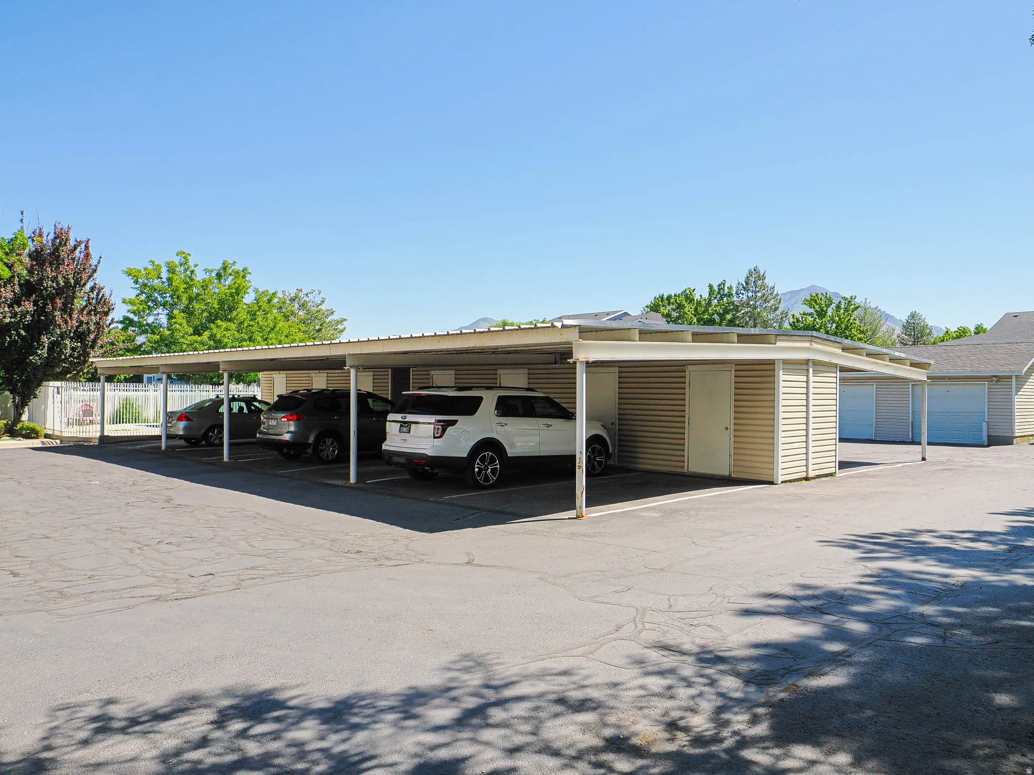 Covered parking structure featuring multiple bays, a light-colored metal roof, and tan horizontal siding on support columns