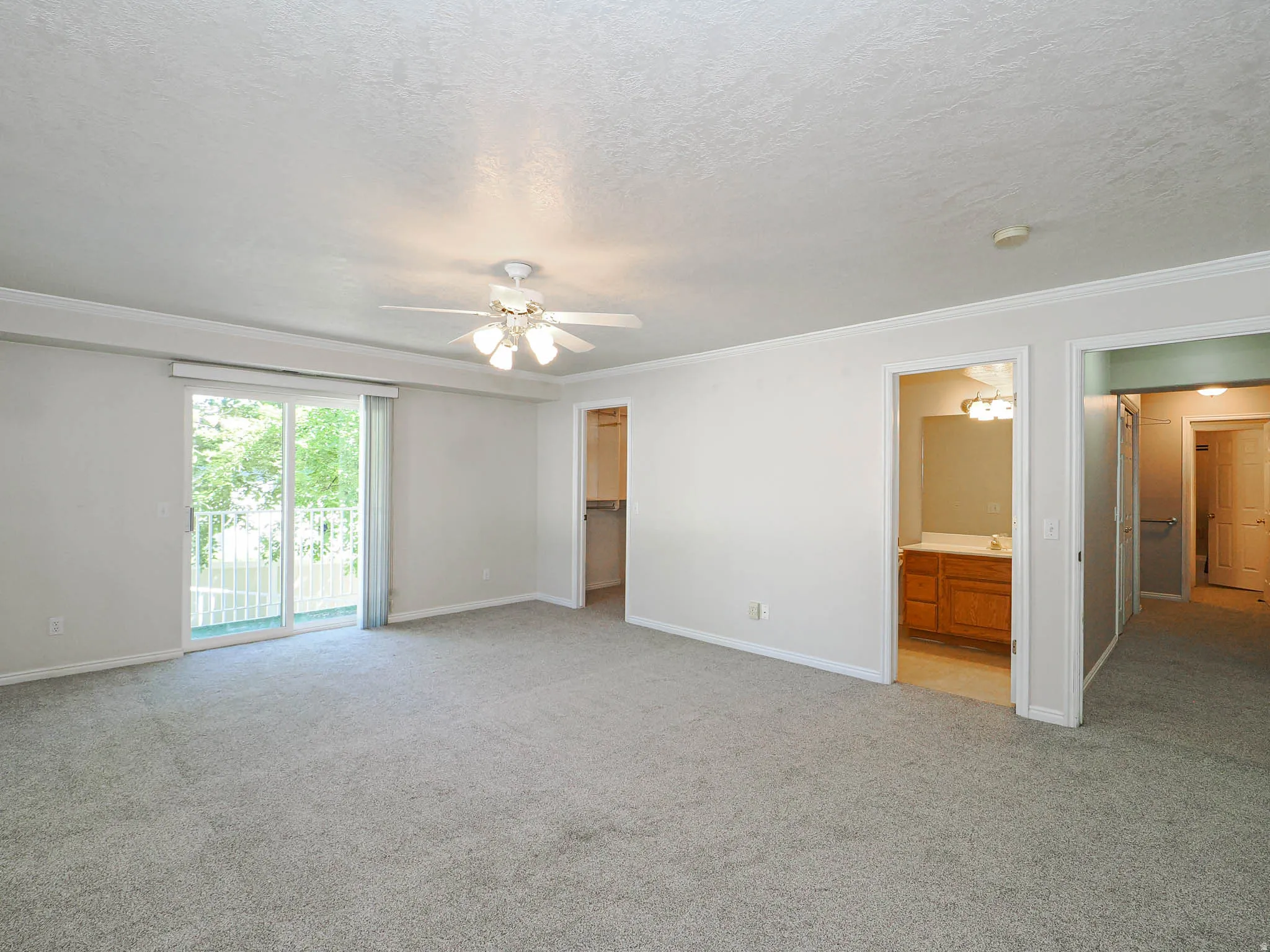 Spacious carpeted room featuring a ceiling fan, crown molding, and a sliding glass door opening to an outdoor balcony