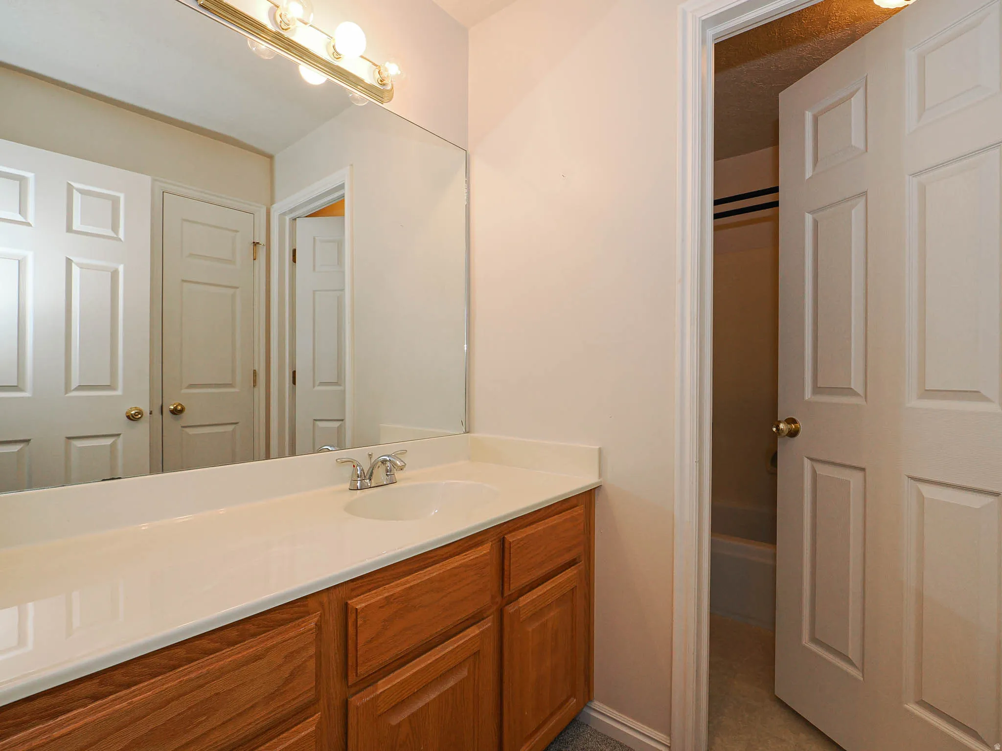 Vanity with light wood cabinetry and a solid surface countertop featuring an integrated white sink and chrome faucet