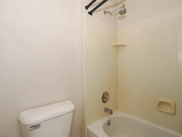 Integrated tub and shower combination featuring a beige surround, chrome fixtures, and a corner shelf