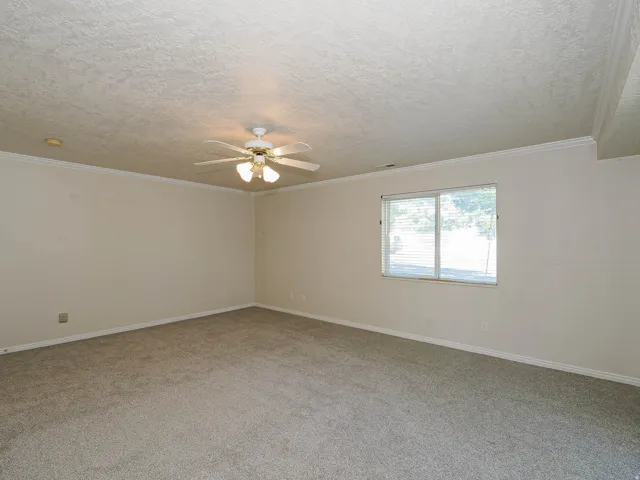 Carpeted interior space featuring a ceiling fan with integrated lighting, crown molding, a window with horizontal blinds, and a recessed light fixture