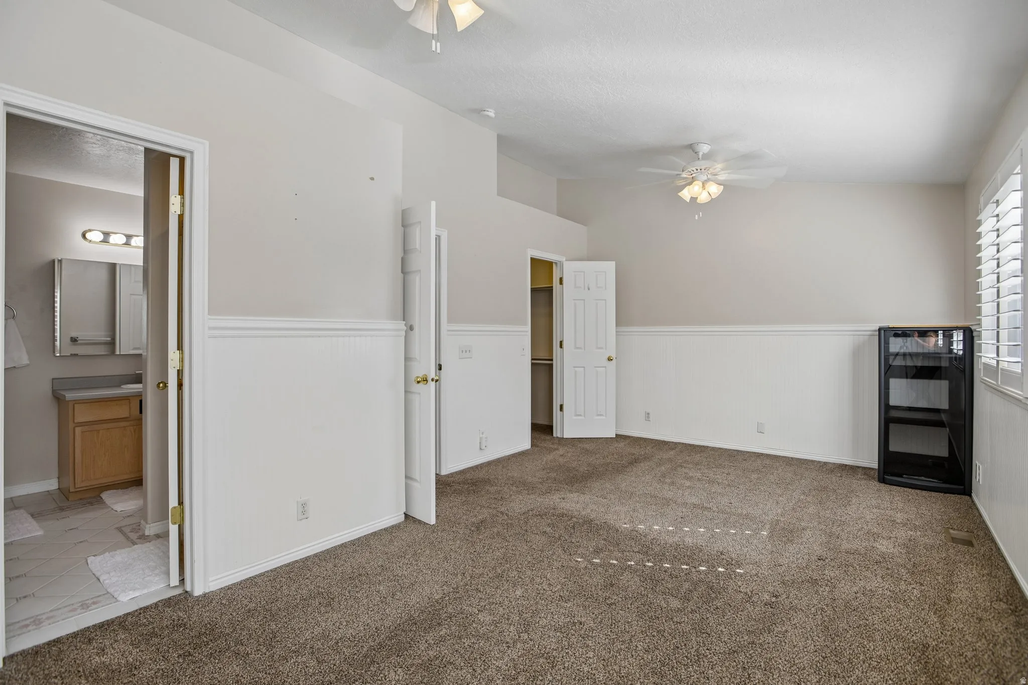 Spacious room featuring vaulted ceilings, ceiling fan light fixture, wainscoting, and carpet flooring