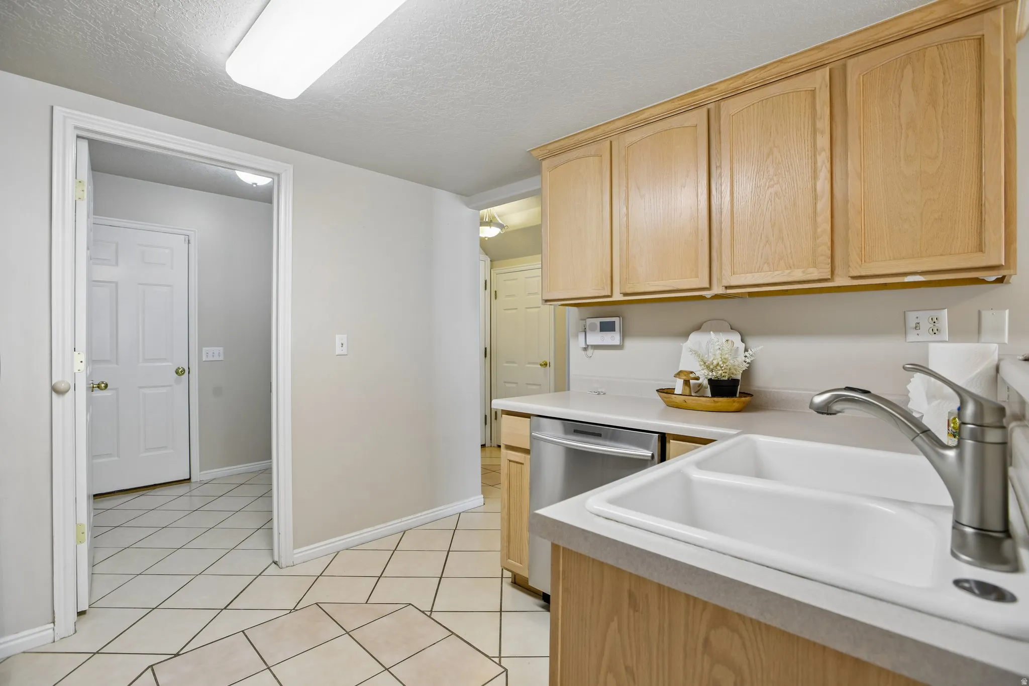 Kitchen area featuring wood cabinetry, a dual-basin sink with brushed nickel faucet, light-toned countertops, and a stainless steel dishwasher