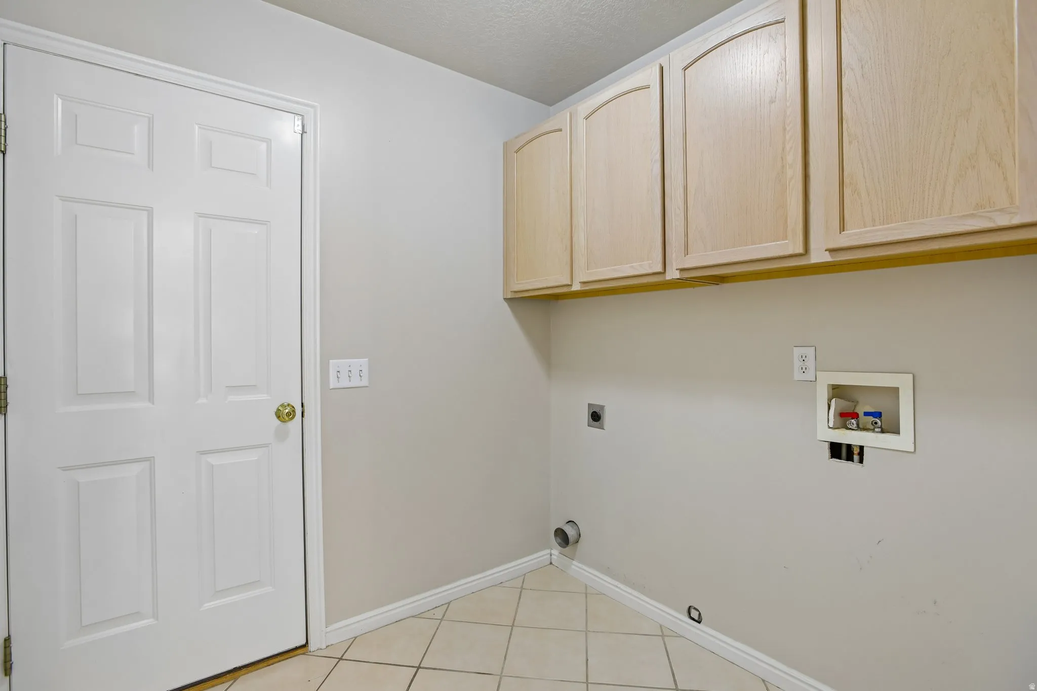 Utility space featuring overhead cabinetry with arched panel doors, tile flooring, and light neutral wall paint