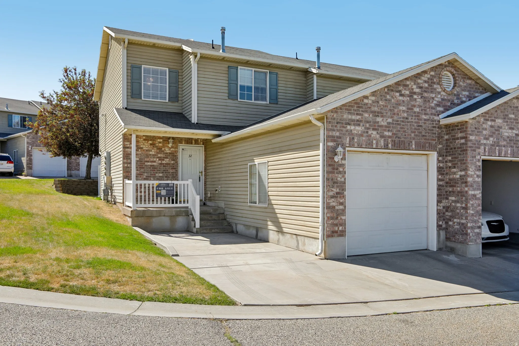 Two-story exterior featuring a brick facade with horizontal siding, an attached single-car garage, a concrete driveway, and a covered entry porch with white railings