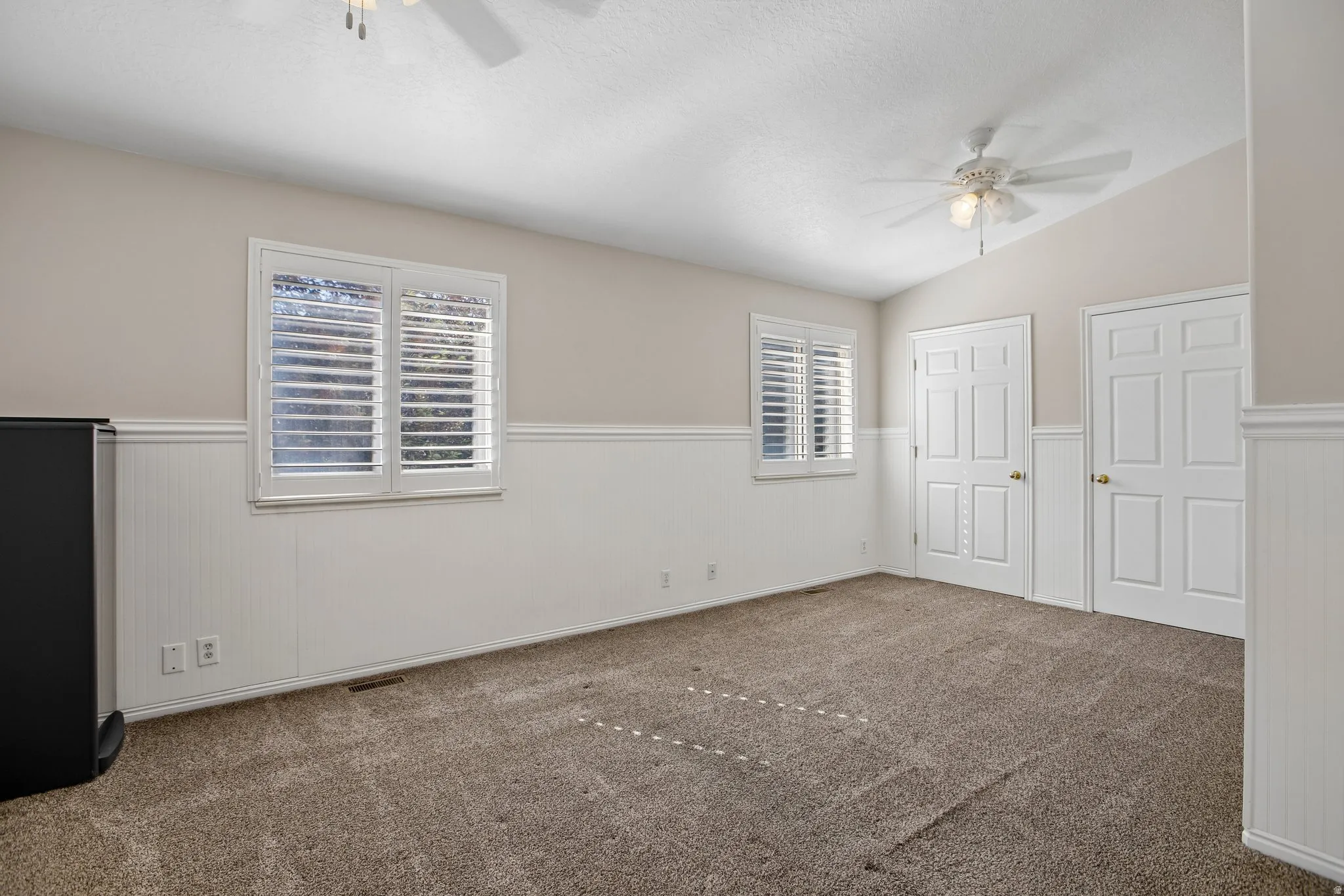 Carpeted room with wainscoting and two windows featuring white louvered shutters