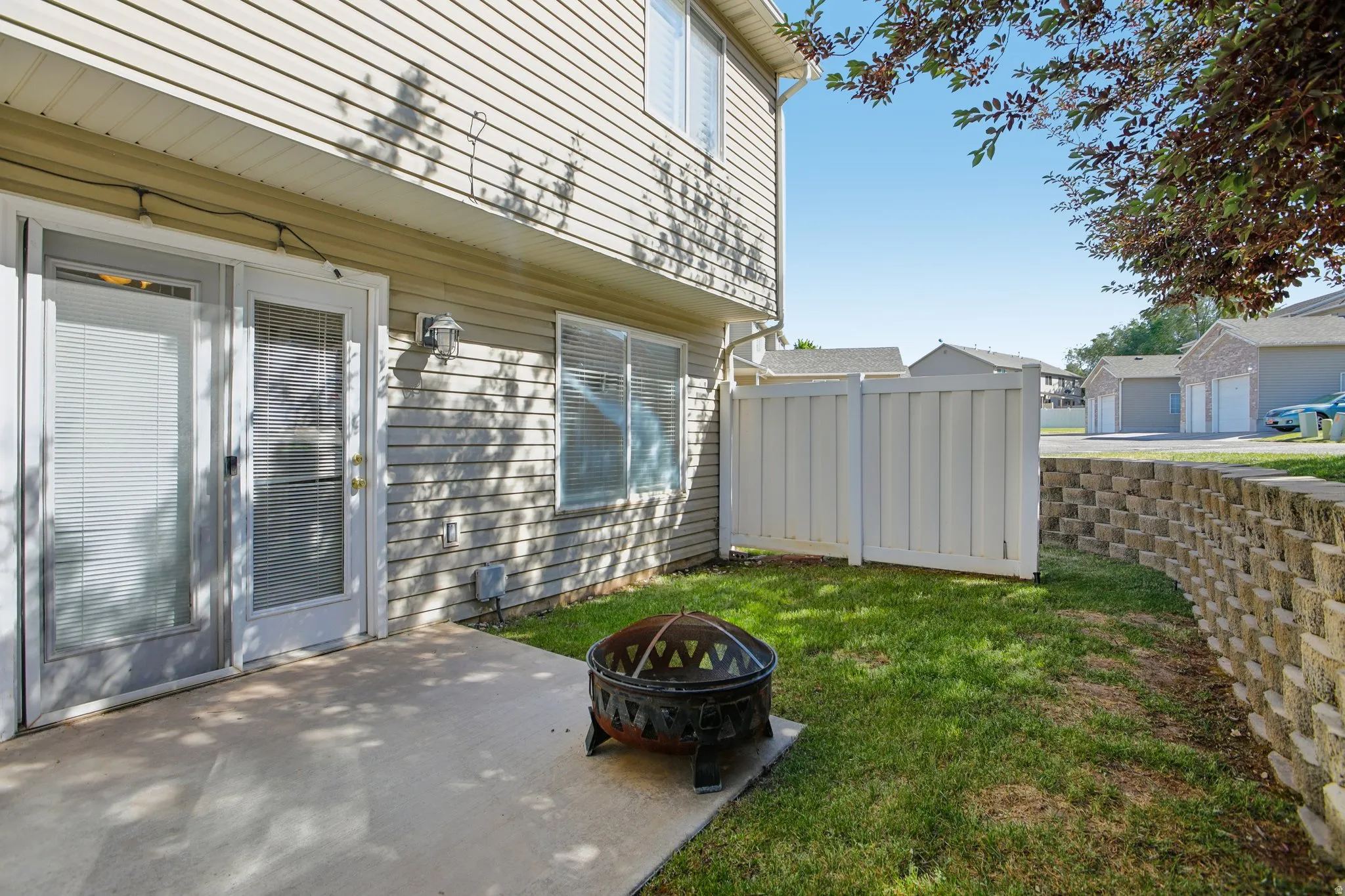 Private backyard patio with a concrete surface, bordered by a retaining wall and green lawn