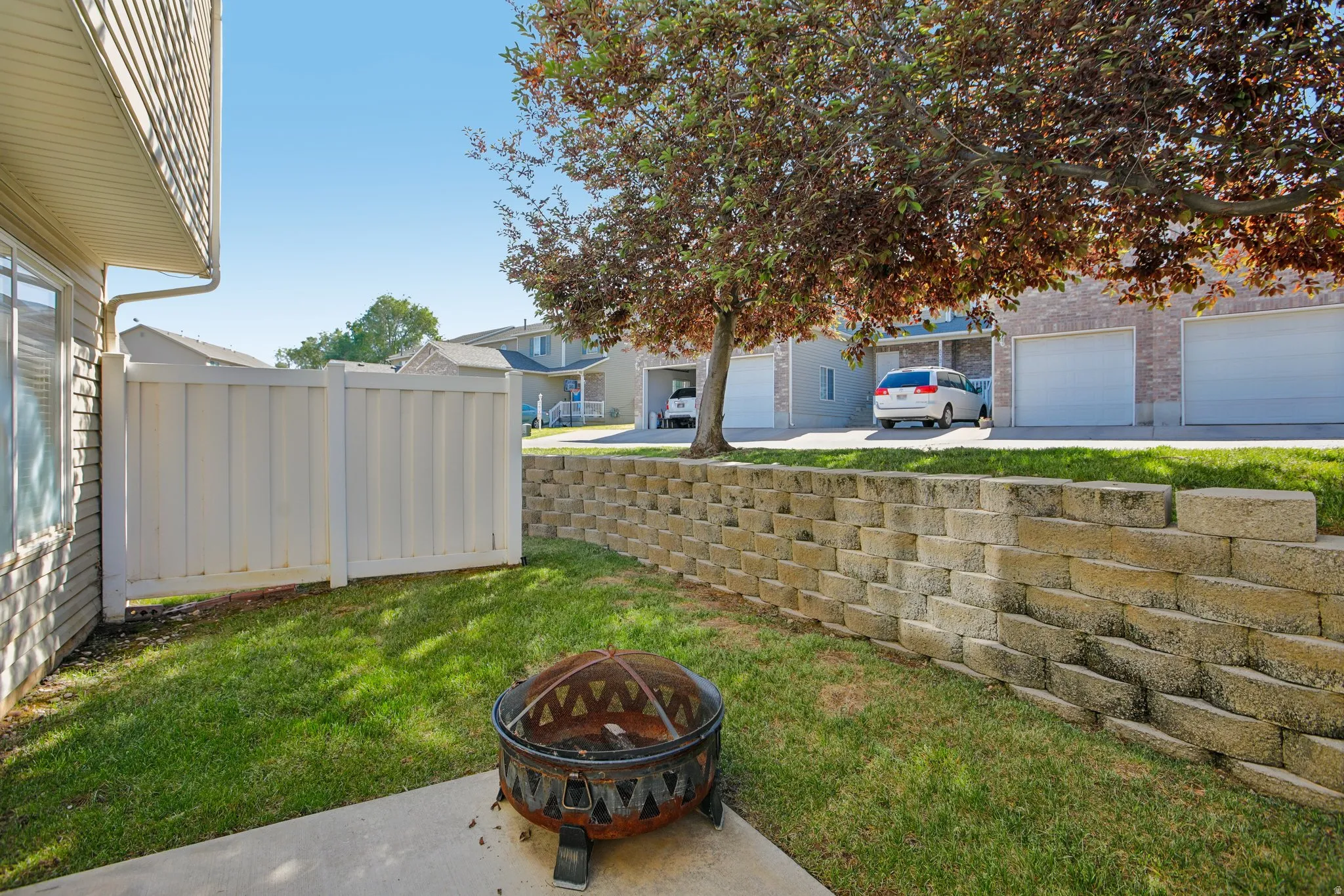 Private fenced patio area featuring a concrete slab, green lawn, and a tiered stone retaining wall