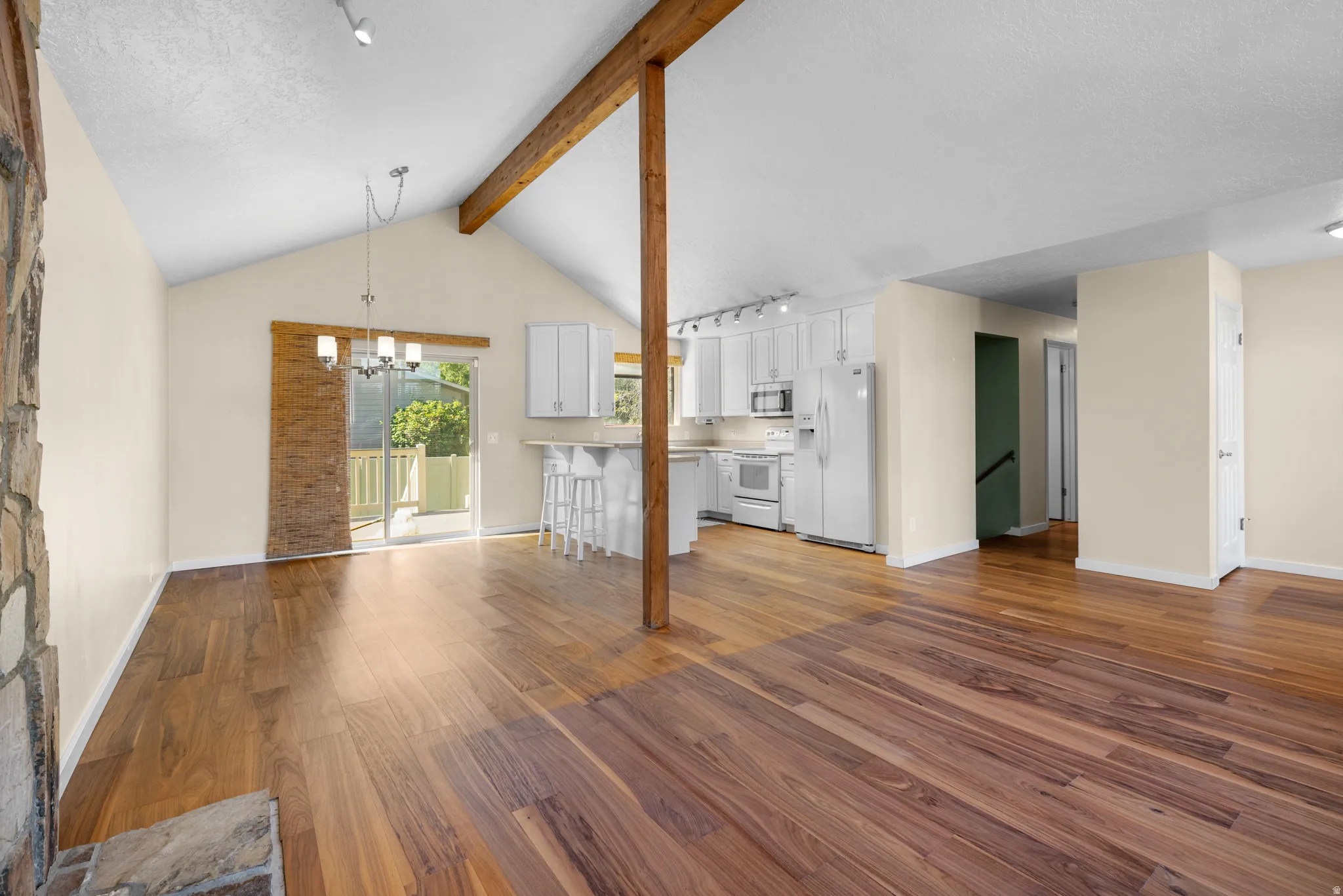 Vaulted ceiling living area with wood-finish flooring, exposed wood beam, stone fireplace, and a sliding glass door