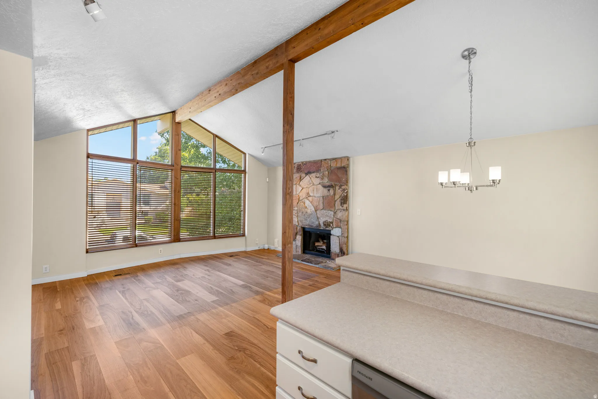 Living area featuring vaulted ceilings with exposed wood beams, extensive window frontage, wood-finish flooring, and a stone fireplace