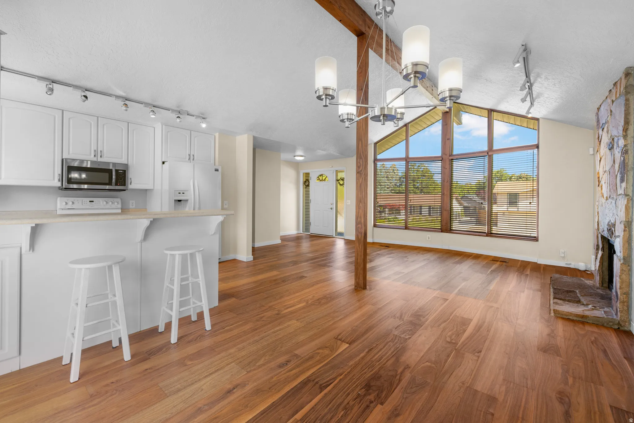 Open-concept living space featuring wood-finish flooring, a stone fireplace, and a large picture window