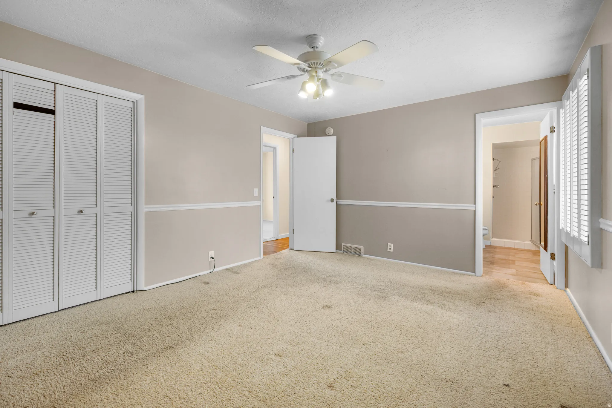 Spacious room featuring neutral paint with chair rail molding, a ceiling fan with integrated lighting, and carpet flooring