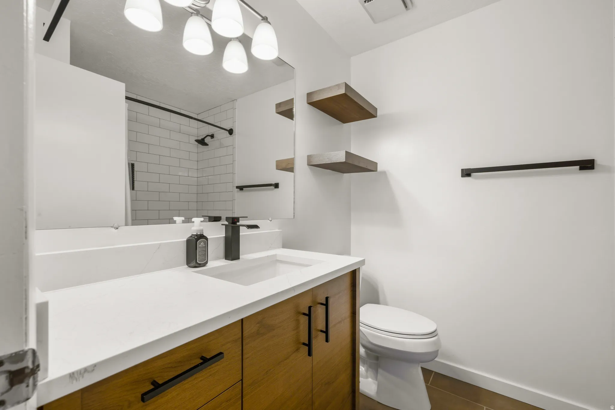 Contemporary bathroom featuring a wood-finish vanity with sleek black hardware, a white countertop, and an integrated sink