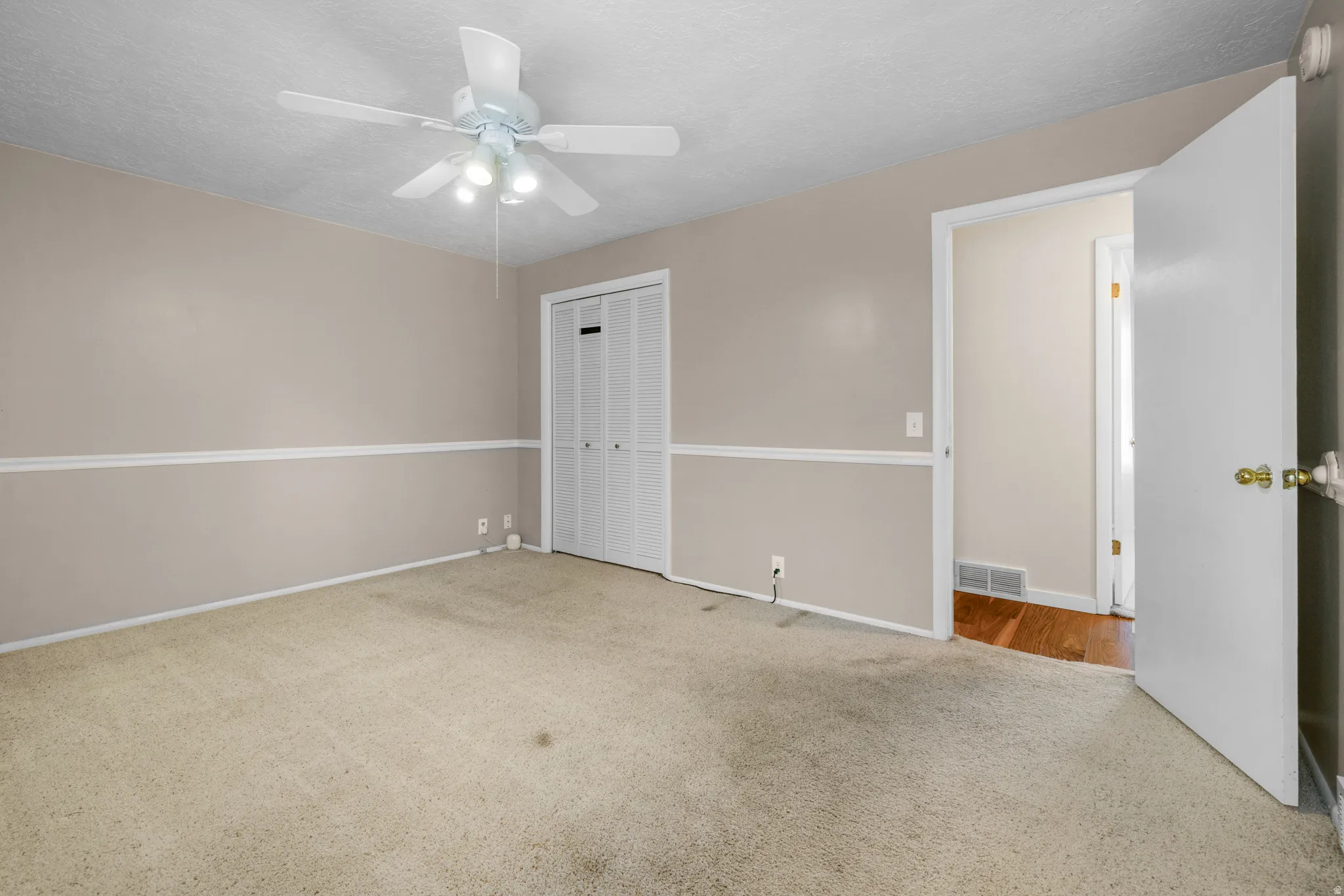 Carpeted room featuring a ceiling fan with integrated lighting, bi-fold closet doors, wall molding, and a neutral color palette