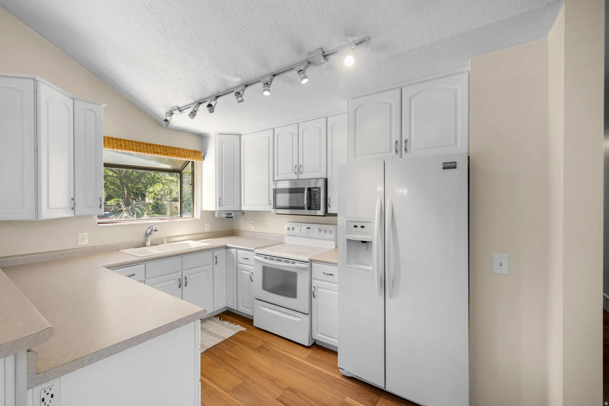 Kitchen featuring white cabinetry, light countertops, wood-finish flooring, and a vaulted ceiling
