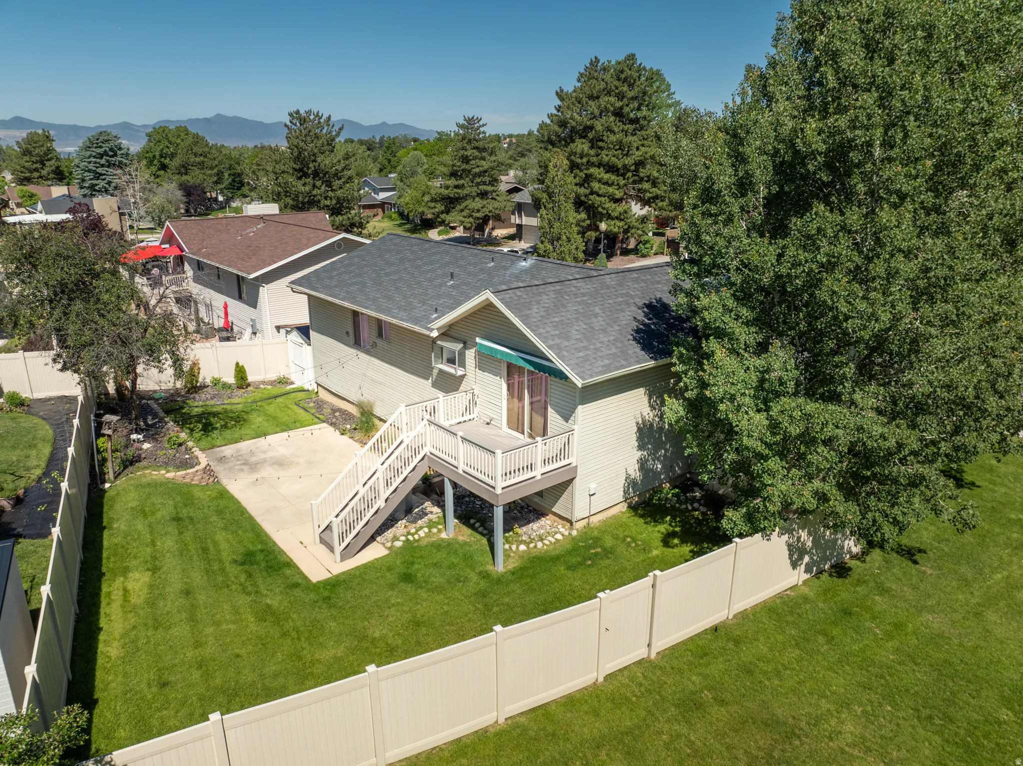 Spacious backyard featuring a multi-level deck, concrete patio, expansive lawn, and full privacy fencing