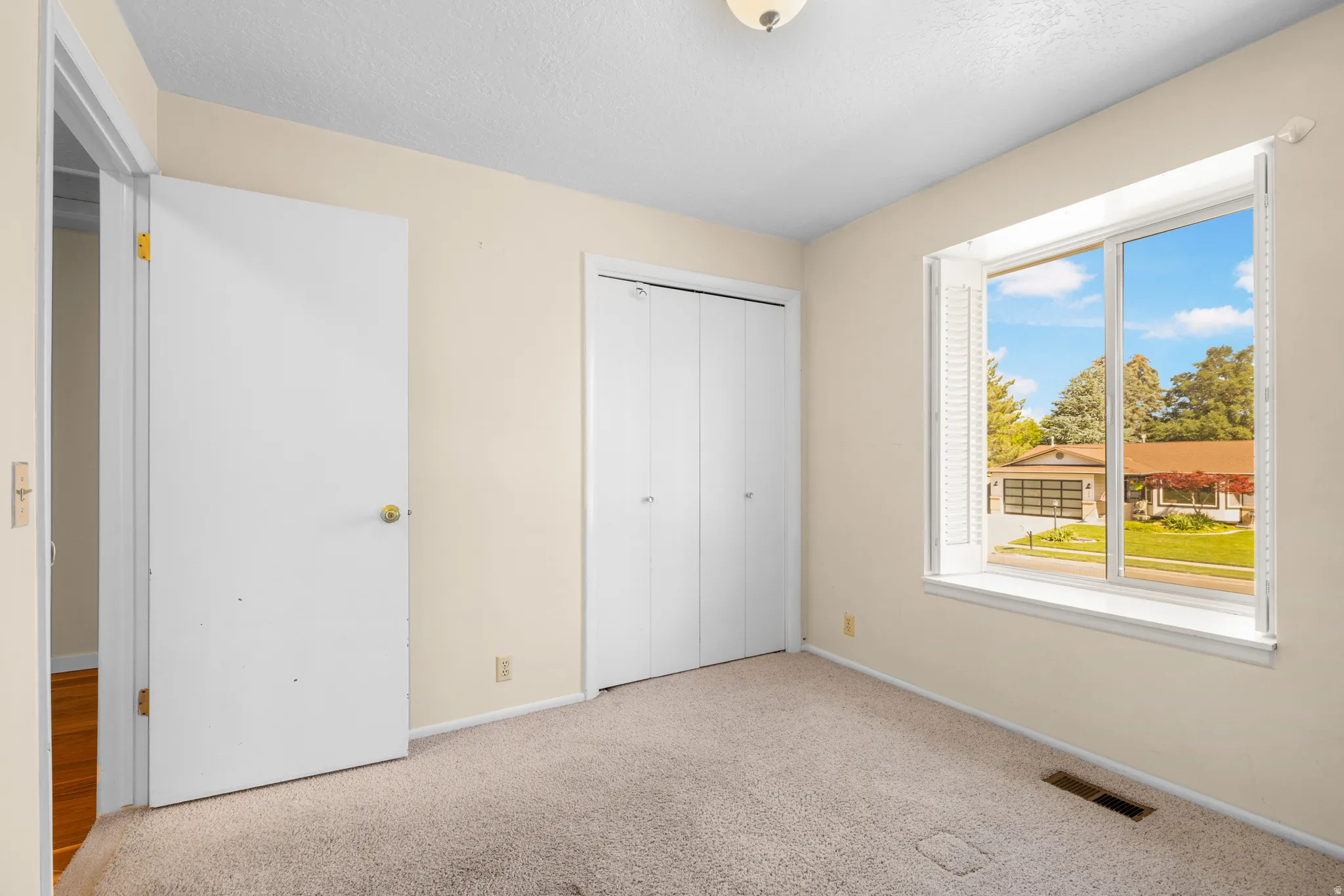 Carpeted room featuring a double window with exterior street scenery, bi-fold closet doors, and an overhead light fixture